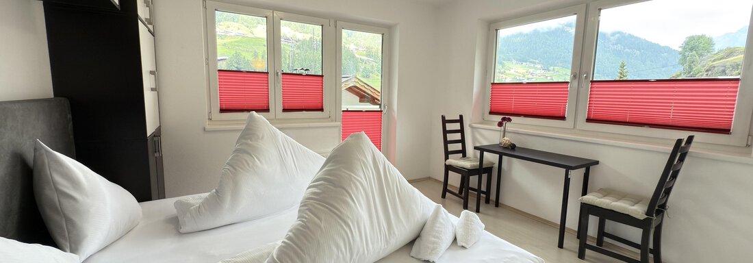 A cozy bedroom with a double bed and two chairs. Large windows provide a view of the surrounding landscape. - Haus PIA by A CASA - Sölden