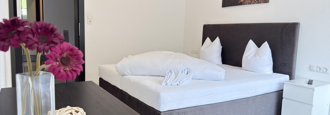A modern bedroom with a large bed and white pillows. On the nightstand are flowers and a decorative ball. - Haus PIA by A CASA - Sölden