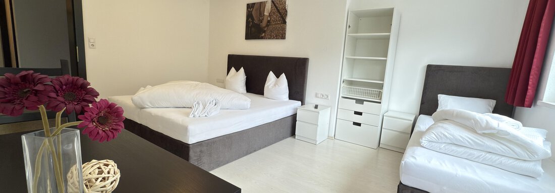 A modern room with two beds and an additional single bed. The room is bright and cheerfully furnished, with a vase full of flowers on the table. - Haus PIA by A CASA - Sölden