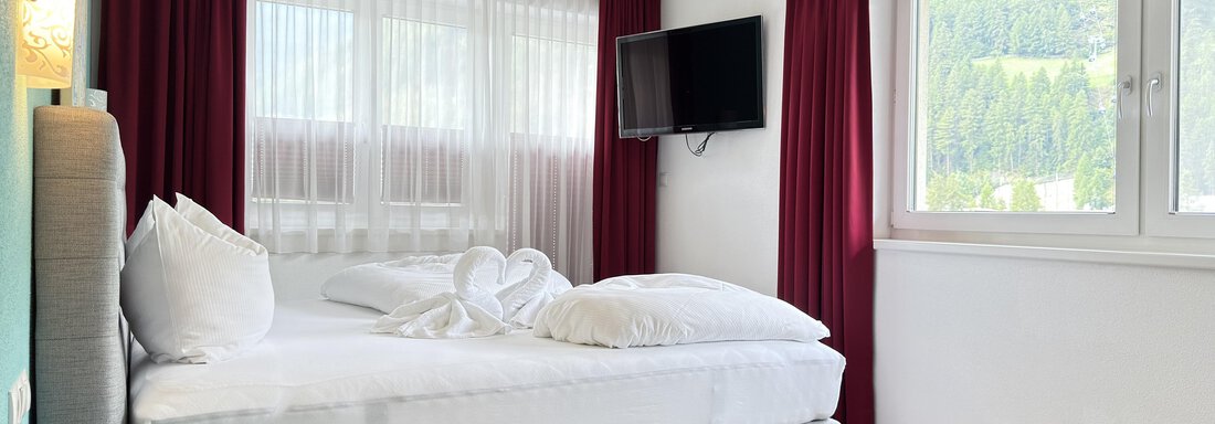 A modern bedroom with a double bed and a television on the wall. Large windows provide plenty of daylight and a view of nature. - Haus PIA by A CASA - Sölden