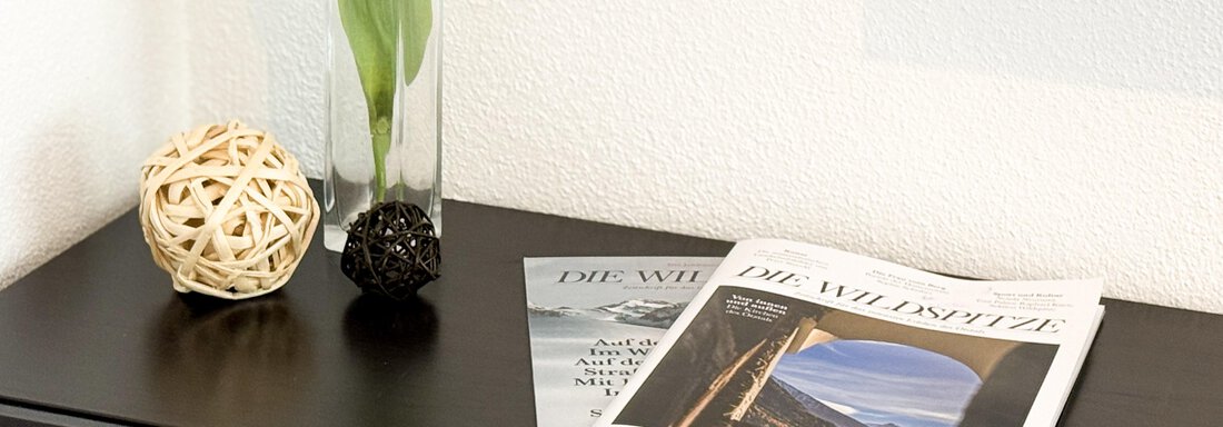 A stylish table with a vase of tulips and a decorative ball. On top of it are two magazines. - Haus PIA by A CASA - Sölden