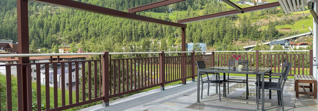 A large terrace with a dining area and a view of the wooded mountains. The sky is cloudy, creating a calm atmosphere. - Haus PIA by A CASA - Sölden