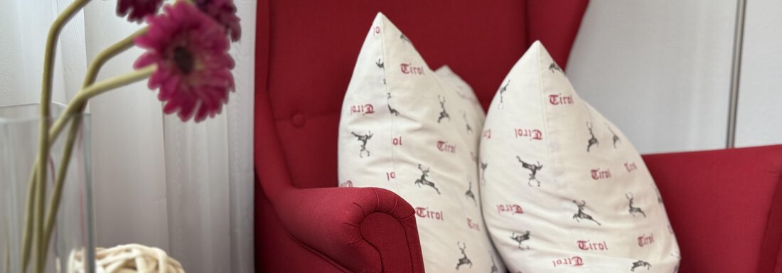 A red armchair with decorative cushions and a table in the foreground. Next to the armchair, there are fresh flowers in a vase. - Haus PIA by A CASA - Sölden