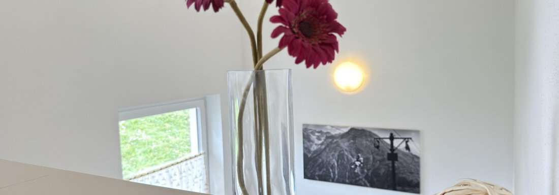A glass vase with pink flowers is on a table. Next to it are decorative balls and a painting in the background. - Haus PIA by A CASA - Sölden