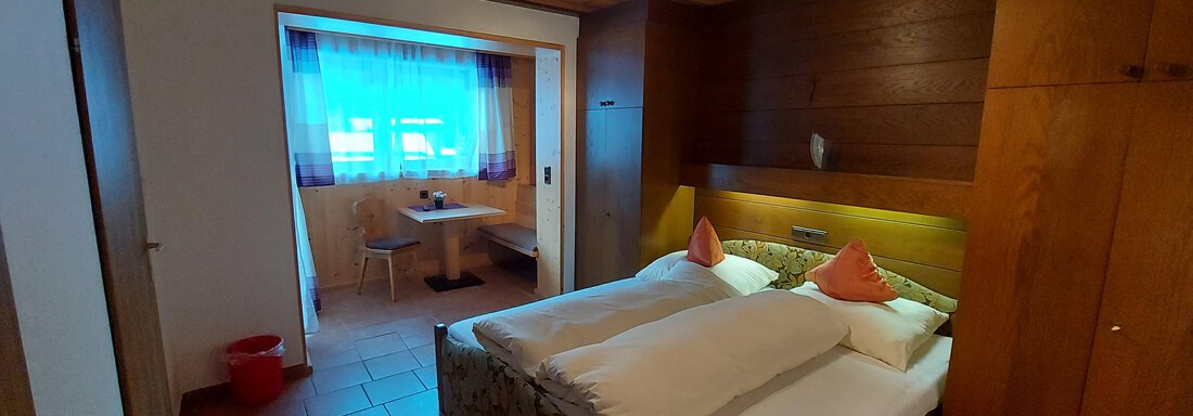 A cozy bedroom with a double bed and wooden walls. Next to the bed is a small table and chairs in front of a window. - Haus Pitzwald - Sölden