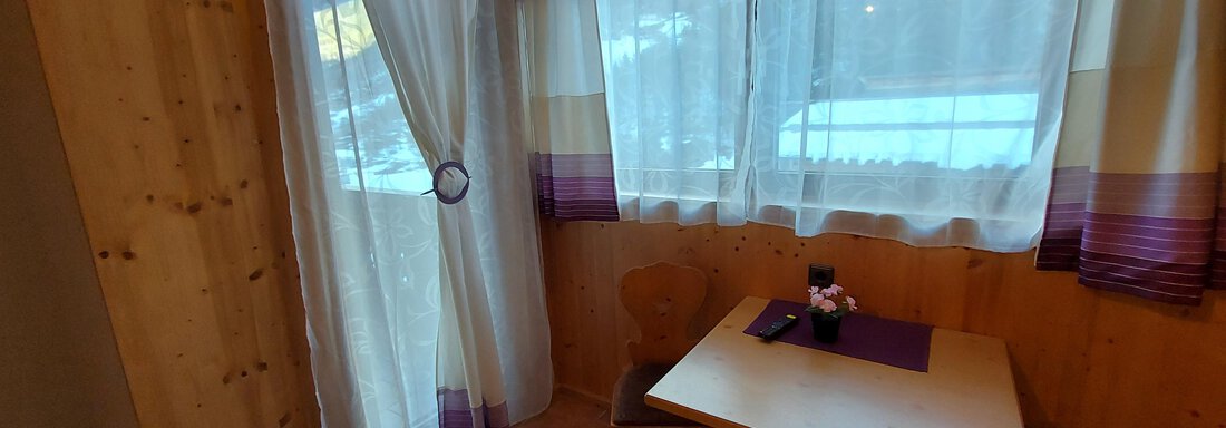 A cozy dining area with a wooden table and chairs. Large windows with curtains let in plenty of light. - Haus Pitzwald - Sölden