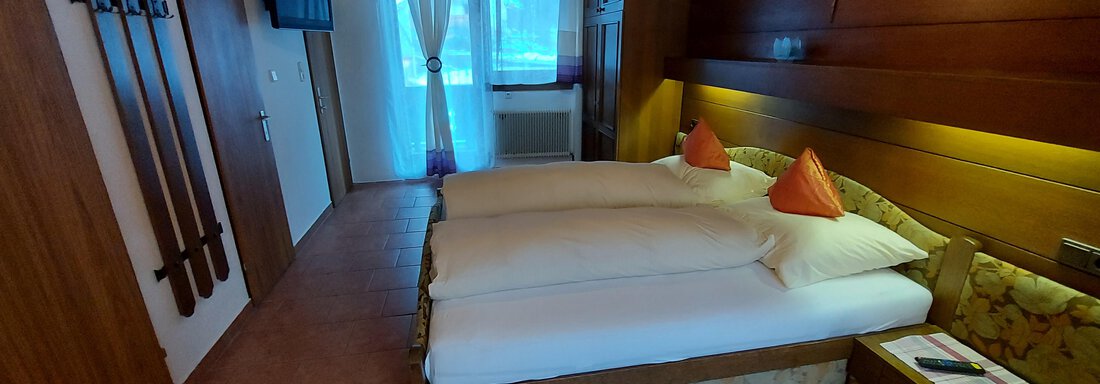 A cozy room with two beds and orange-colored pillows. Ski pads are hanging on the wall and the room has large windows with a view outside. - Haus Pitzwald - Sölden