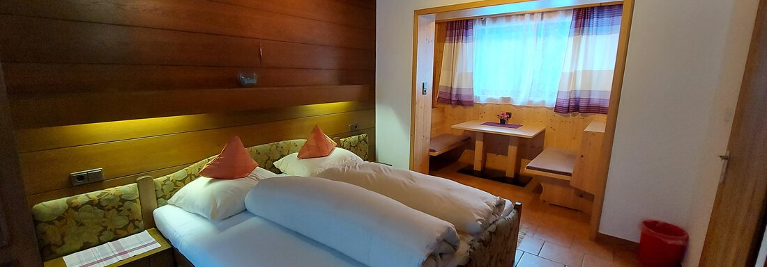 A cozy room with two beds and a bright window front. The wooden paneling and warm colors create an inviting atmosphere. - Haus Pitzwald - Sölden