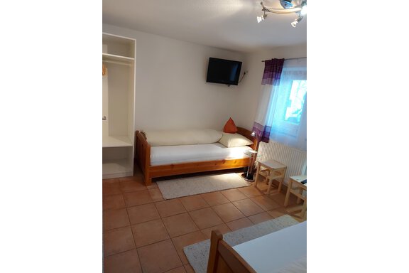 A simple room with a bed, a television, and a white sofa. There is a table with two chairs and plenty of natural light coming through the window. - Haus Pitzwald - Sölden