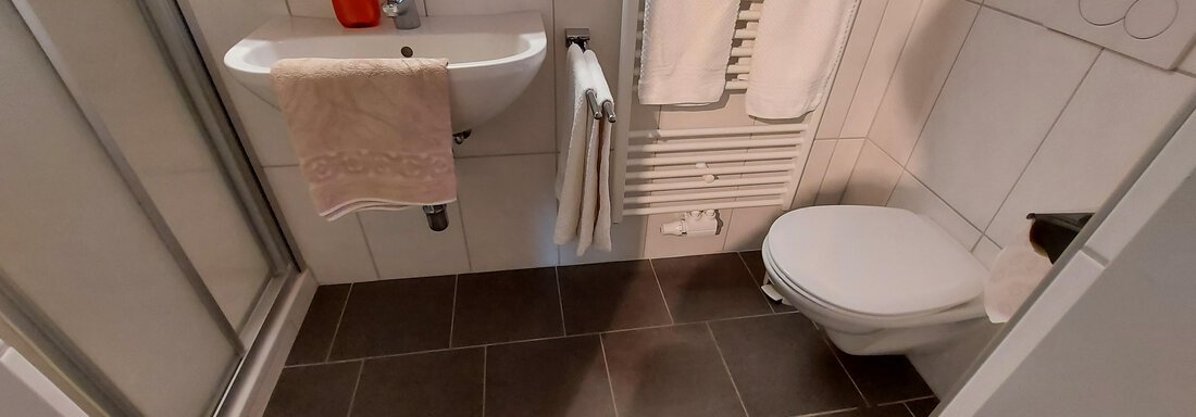 A modern bathroom with a shower, sink, and toilet. The walls are tiled in a light color and there are towels and a towel rack. - Haus Pitzwald - Sölden