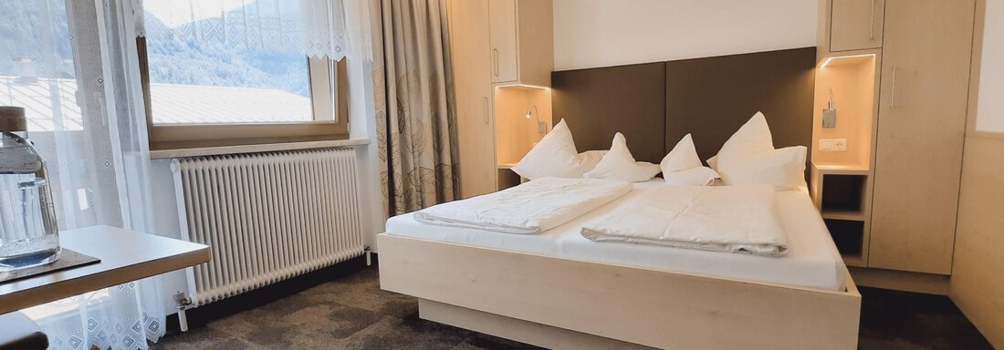 A modern and cozy bedroom with a large bed and elegant furniture. The windows offer a view of the surrounding mountain landscape. - Haus Rehwinkl - Sölden