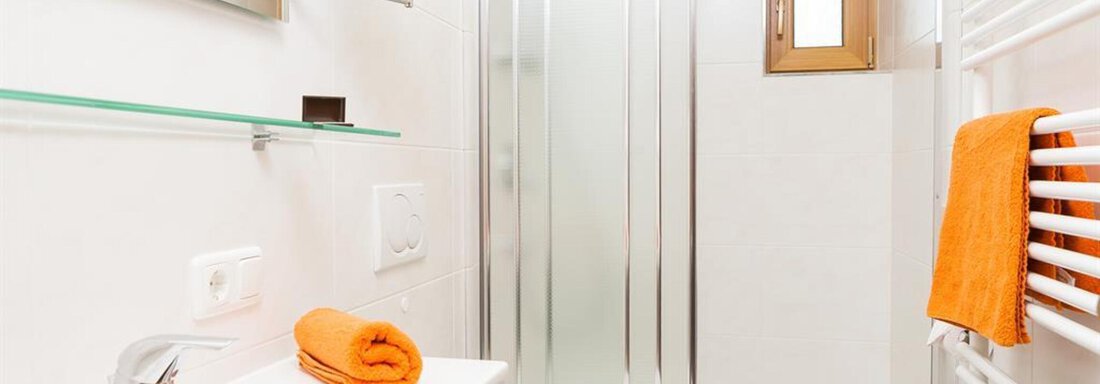 A modern bathroom with a shower, sink, and a large mirror. Orange towels complement the bright, clean design. - Haus Rehwinkl - Sölden