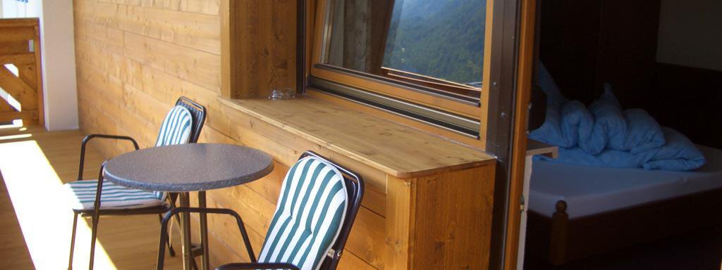 A cozy balcony with two chairs and a round wooden table. In the background, a bedroom with a visible bed can be seen. - Haus Rehwinkl - Sölden