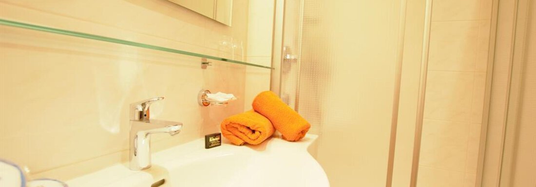 A modern bathroom with a sink and a shower. On the sink lies an orange towel. - Haus Rehwinkl - Sölden