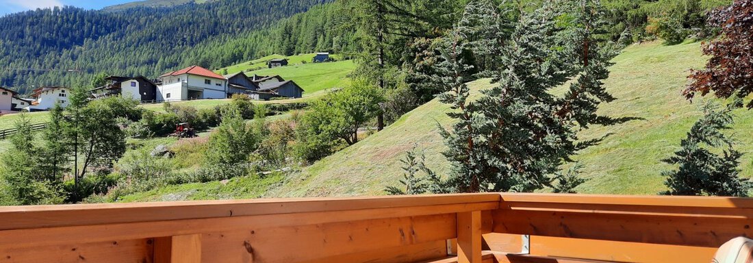 A beautiful view from a wooden balcony over green meadows and mountains. In the background, some houses can be seen. - Haus Rehwinkl - Sölden