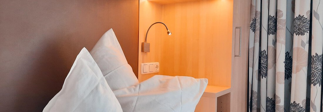 A cozy bedroom with two white pillows and soft lighting. The walls are in neutral colors and there are decorative curtains. - Haus Rehwinkl - Sölden