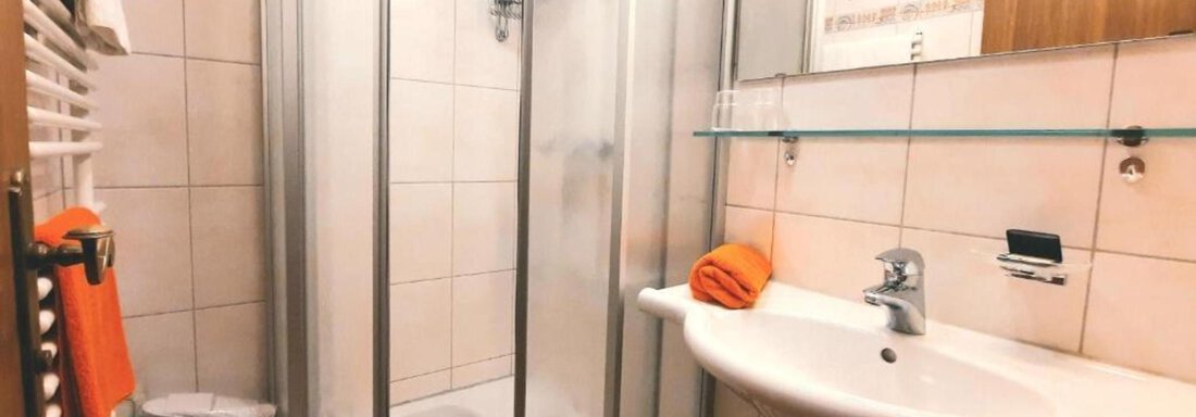 A modern bathroom with a shower cabin and a sink. Towels in orange and a bright tiled wall give the room a cheerful atmosphere. - Haus Rehwinkl - Sölden