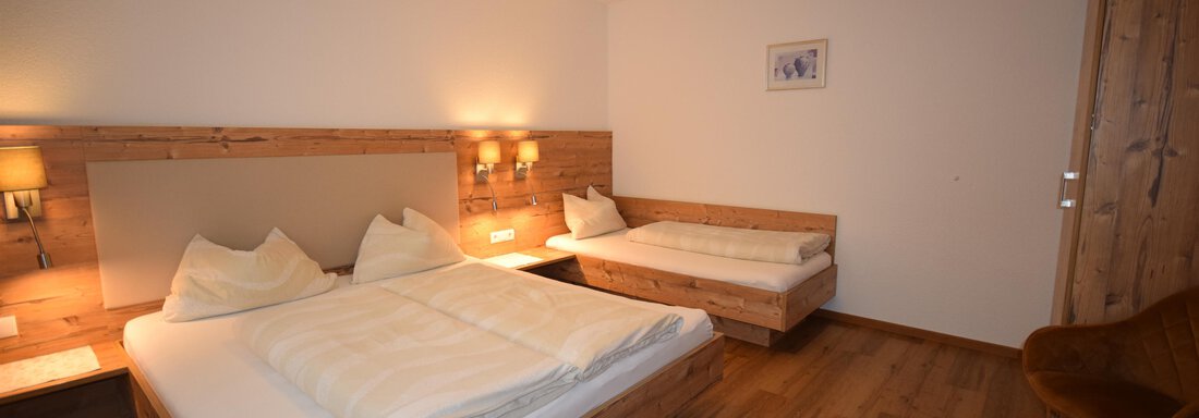 App1 SZ A cozy bedroom with two beds and a single sleeping area. The walls are light, and the floor is made of wood, creating a warm atmosphere. - Haus Romana - Sölden