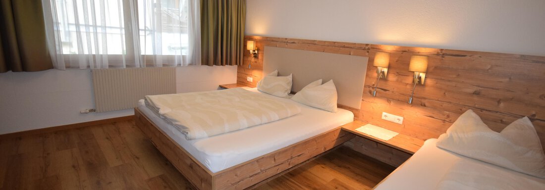 A cozy bedroom with two beds and warm wooden furniture. The windows let in plenty of daylight and the walls are painted in light colors. - Haus Romana - Sölden