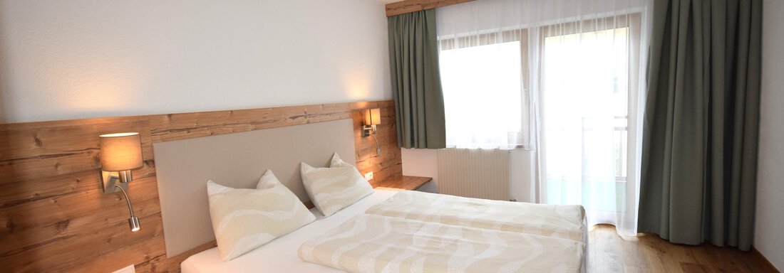 A cozy bedroom with a double bed and wooden paneling. Large windows let in plenty of light and provide a view outside. - Haus Romana - Sölden