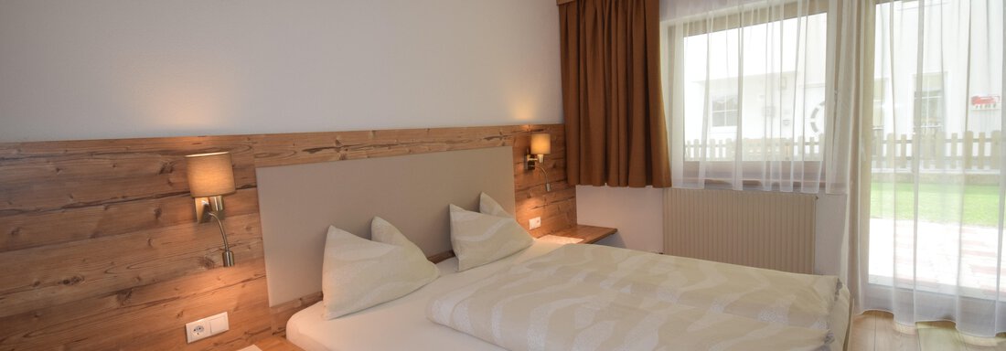 A modern bedroom with a large bed and wooden paneling.  
Large windows provide plenty of daylight. - Haus Romana - Sölden