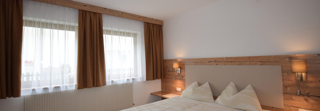 A modern bedroom with a double bed and light wooden decor. Large windows with curtains provide plenty of natural light. - Haus Romana - Sölden