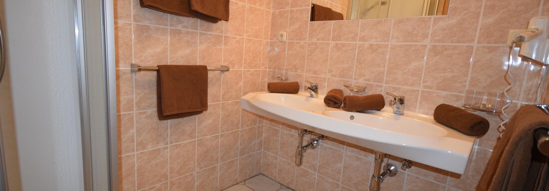 A modern bathroom with tiles in soft colors. Towels and two sinks are visible. - Haus Romana - Sölden