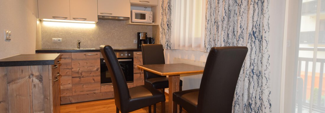 A modern kitchen with wooden furniture and a table for four people. The room has plenty of light from the windows and a cozy atmosphere. - Haus Romana - Sölden