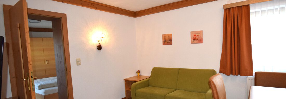 A cozy living room with a green sofa and a table. The walls are bright, and there are wooden embellishments as well as pictures. - Haus Romana - Sölden