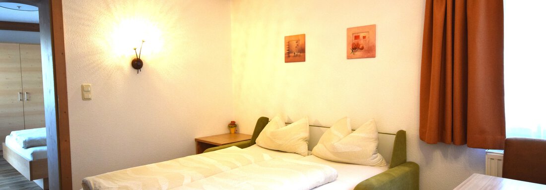 A cozy bedroom with a double bed and two pillows. The walls are light, and there are orange curtains as well as some decorative pictures. - Haus Romana - Sölden