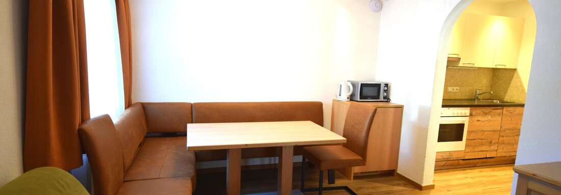 A cozy living room with a dining table and a seating area. The open kitchen is well-equipped and filled with light. - Haus Romana - Sölden
