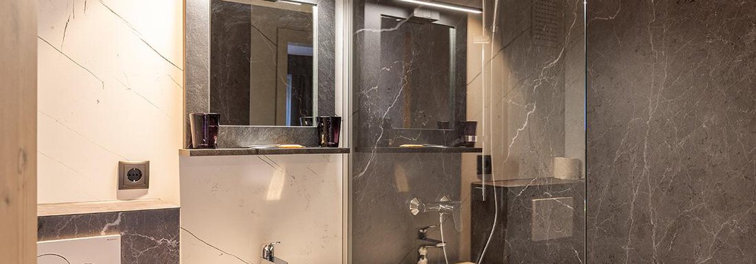 A modern bathroom with stylish black and white tiles. The sink and mirror are elegantly and functionally furnished. - Haus Sieglinde Color - Sölden