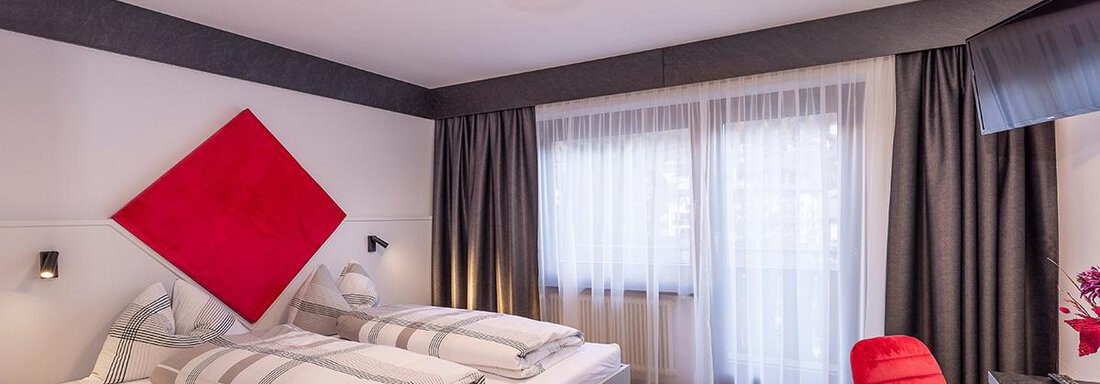 A modern hotel room with two beds and elegant furnishings. Large windows let in plenty of daylight, and a red decoration adds a stylish touch. - Haus Sieglinde Color - Sölden