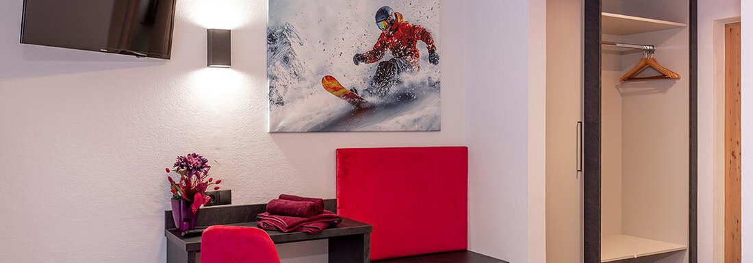 A modern hotel room with a television and a seating area. A picture of a snowboarder in action hangs on the wall. - Haus Sieglinde Color - Sölden
