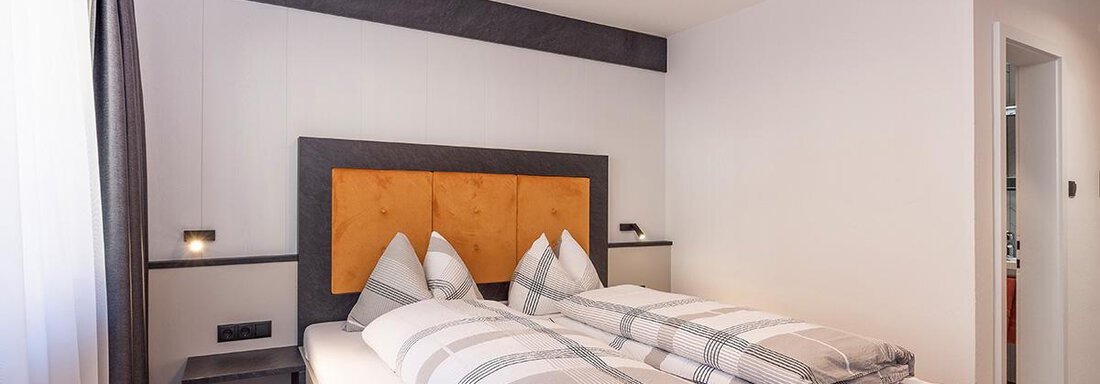 A modern bedroom with two single beds and striped bedspreads. The walls are light and there are large windows with curtains. - Haus Sieglinde Color - Sölden