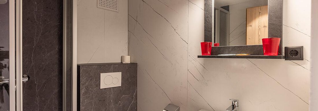A modern bathroom with a shower and a sink. The walls are designed in elegant gray, and there is a lit mirror. - Haus Sieglinde Color - Sölden
