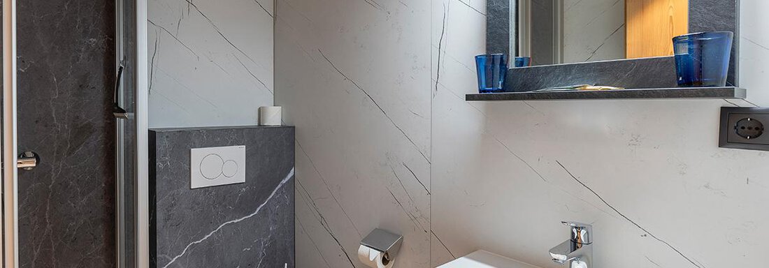A modern bathroom with elegant gray tiles and a large mirror. The sink is spacious and the fixtures look stylish and functional. - Haus Sieglinde Color - Sölden