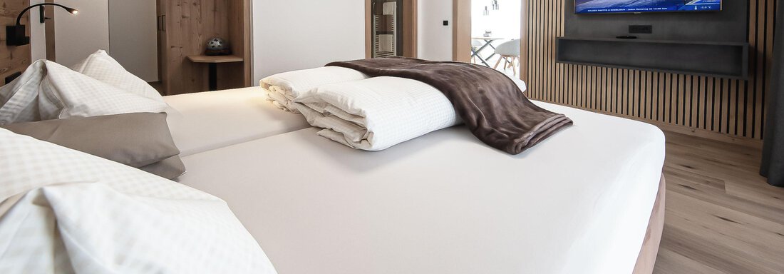 A modern bedroom with a double bed and soft pillows. A TV hangs on the wall, and the room has a bright, inviting look. - Haus Sonnwend - Sölden