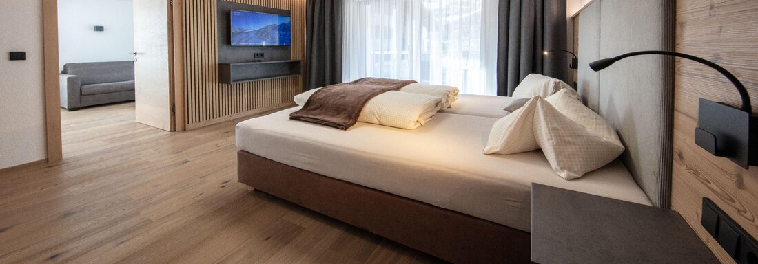 Zimmer | © CI-CENTER (CC C) A modern bedroom with a large bed and wooden floor. A comfortable atmosphere with daylight and a seating area. - Haus Sonnwend - Sölden