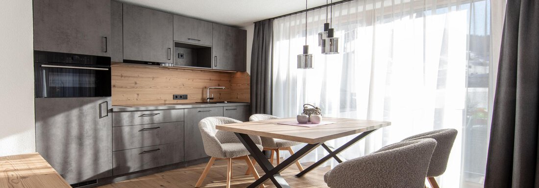 A modern kitchen with a bright dining area. The space features wood and gray elements and has large windows that let in plenty of light. - Haus Sonnwend - Sölden