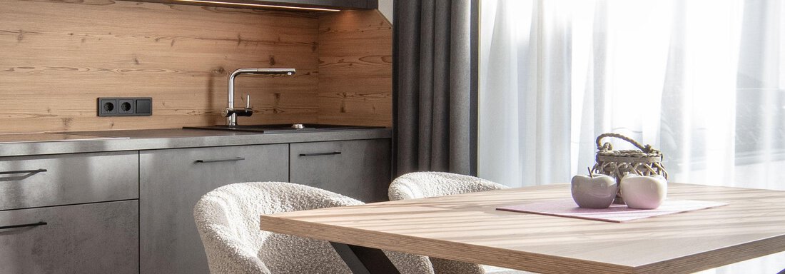 A modern kitchen corner with wooden walls and gray furniture. The table is made of wood and has decorative plants on it. - Haus Sonnwend - Sölden
