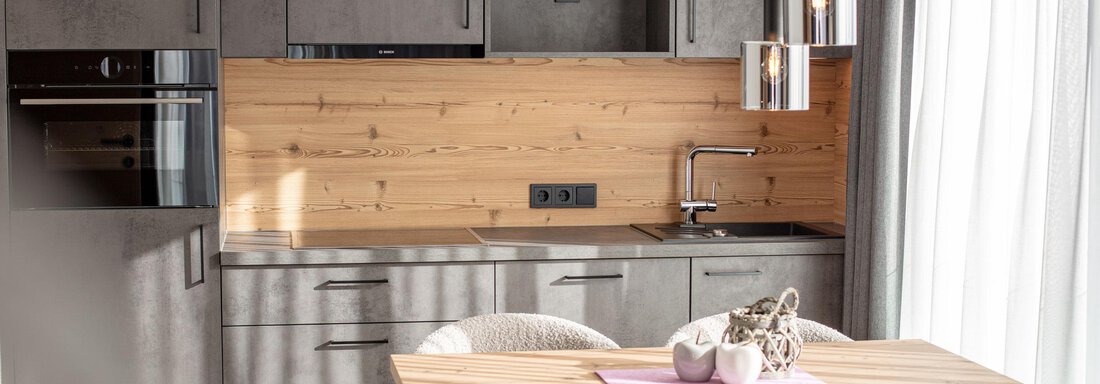 A modern kitchen with wood and metal accents. A wooden table stands in the middle, surrounded by comfortable chairs. - Haus Sonnwend - Sölden