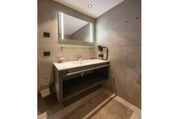 A modern bathroom with an elegant sink setup and a large mirror. The walls are painted in neutral tones, giving the space a contemporary flair. - Haus Sonnwend - Sölden