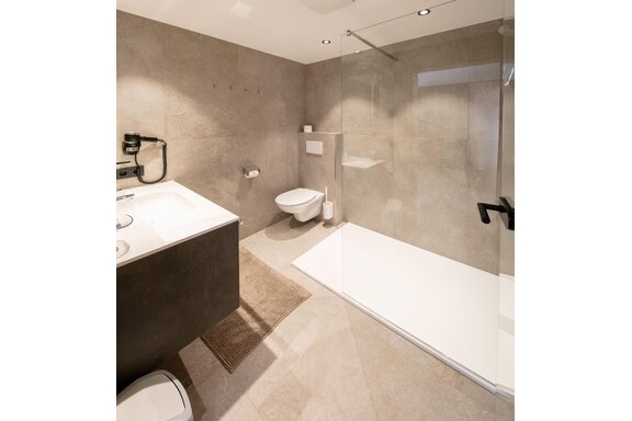 A modern bathroom with a shower and an elegant sink. The walls are in neutral gray tones. - Haus Sonnwend - Sölden