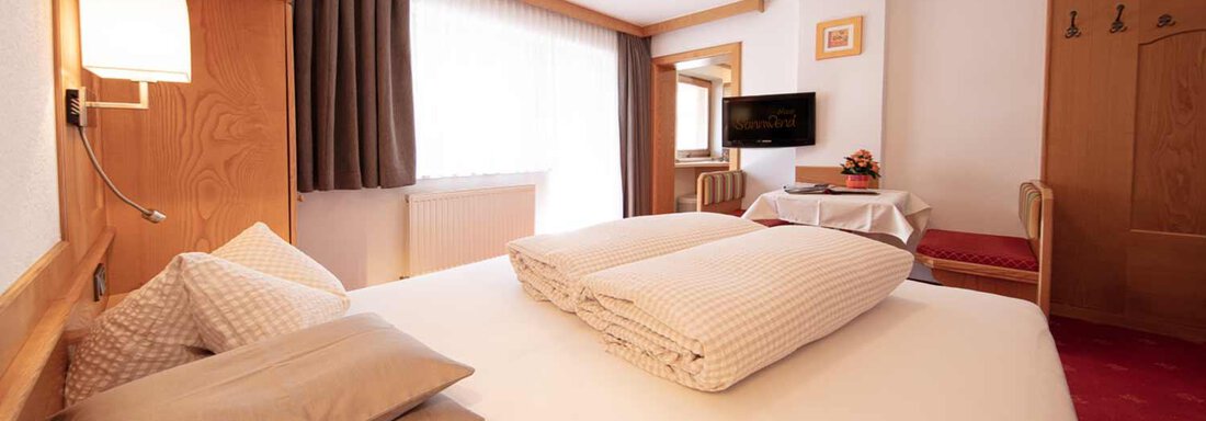A cozy bedroom with a large bed and soft pillows. The room is bright and furnished in a modern style, with a television and a small table. - Haus Sonnwend - Sölden