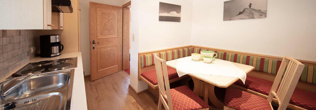 A cozy kitchen with a dining area and wooden chairs. The room has bright walls and a pleasant atmosphere. - Haus Sonnwend - Sölden