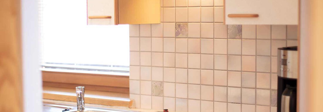 A modern kitchen with a bright tiled splashback and a stove. On the countertop, there are a sink and a coffee machine. - Haus Sonnwend - Sölden