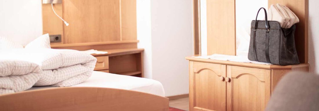 A cozy room with a double bed and wooden shelves. On the dresser, there is a bag, and the room is well-lit. - Haus Sonnwend - Sölden