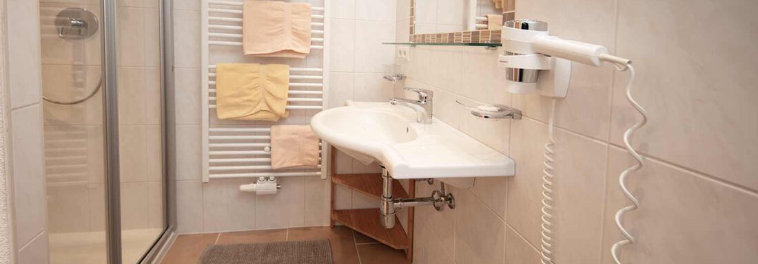 A modern bathroom with a shower and a sink. Towels are neatly hung on a holder, and the floor is tiled. - Haus Sonnwend - Sölden