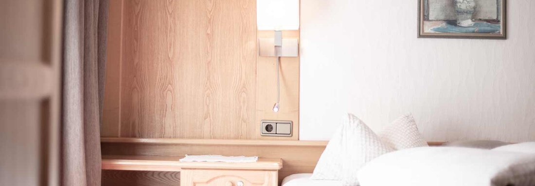 A cozy room with wooden details and warm colors. On the table, there is a vase with flowers, and there is a comfortable bed with pillows. - Haus Sonnwend - Sölden